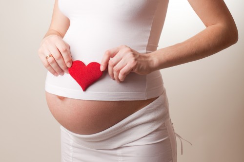 Беременная женщина держит у живота красное сердце